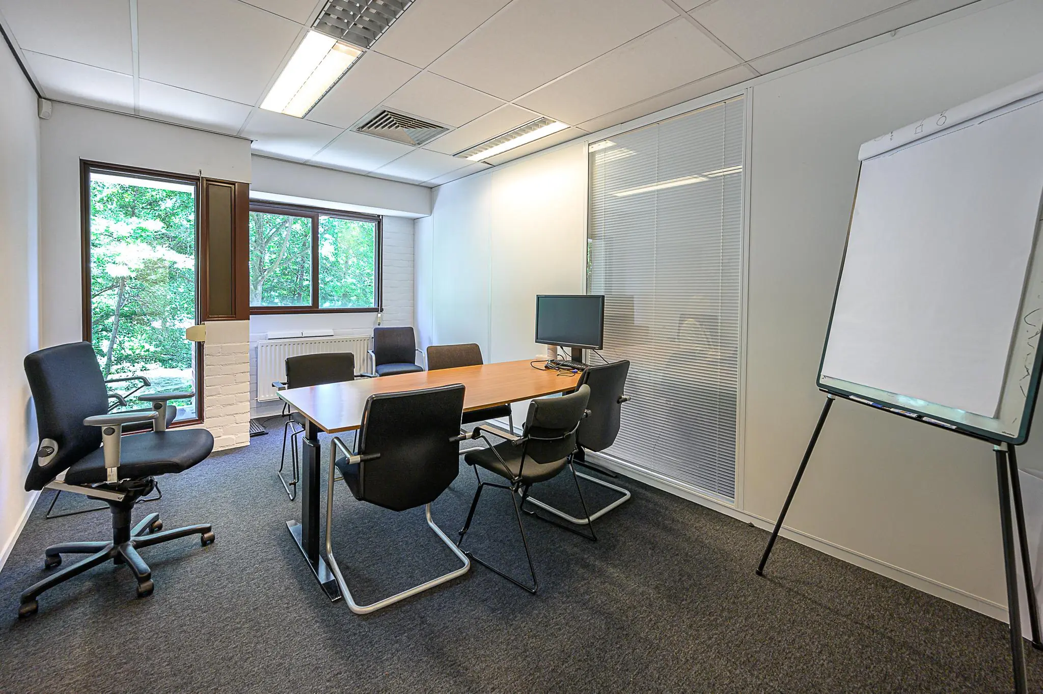 Vergaderruimte De Linie met een tafel, zes stoelen, een flip-over en een computerscherm bij het raam.